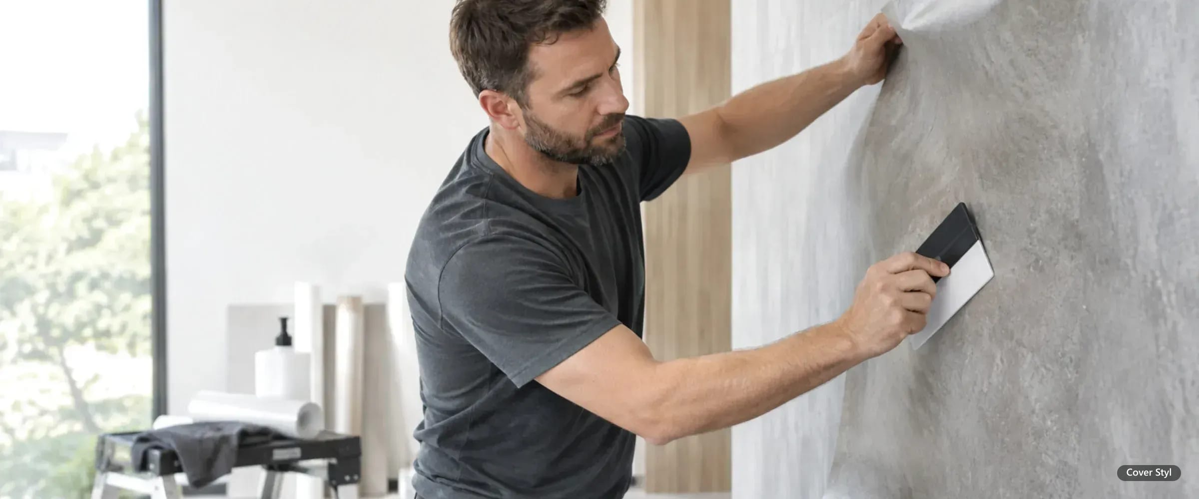 Installateur zieht eine Cover Styl Architekturfolie in grauer Steinoptik mit dem Rakel auf eine Wand auf
