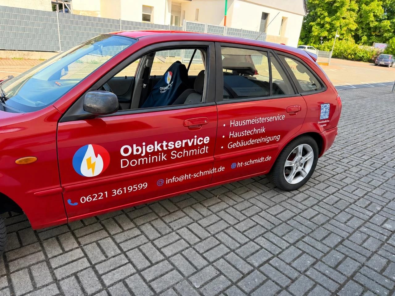 Roter Mazda mit Fahrzeugbeschriftung: Logo, Leistungen, Telefonnummer, E-Mail und Web-Adresse auf der Fahrerseite